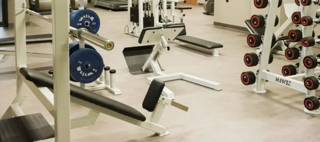A hotel gym: benches, a barbell with plates and a dumbbell rack